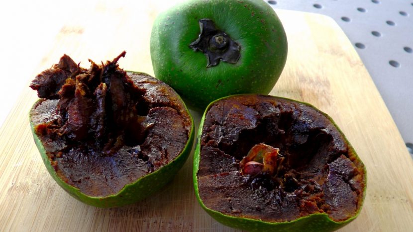 Fruto de zapote negro partido por la mitad con la pulpa oscura