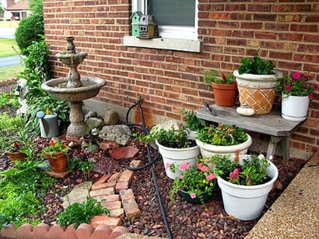 Jardín pequeño con fuente, plantas en distintos niveles y pavimento continuo